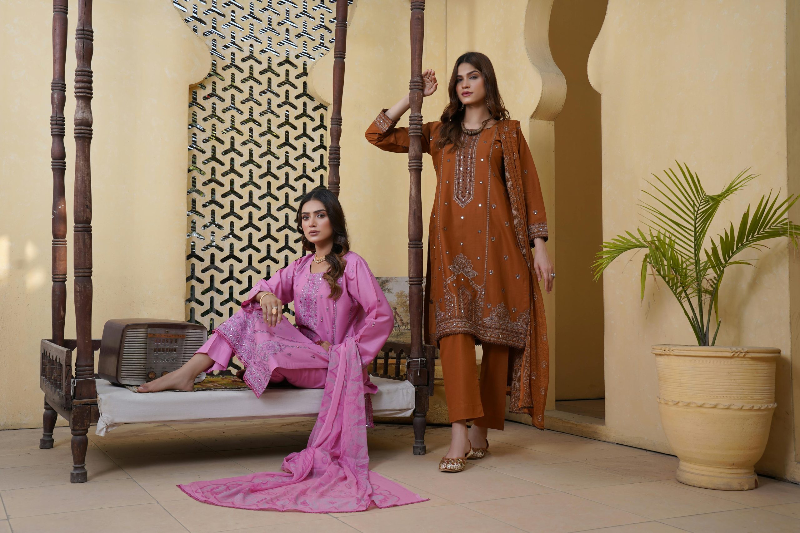 Two women in traditional clothing pose elegantly in a Lahore setting.